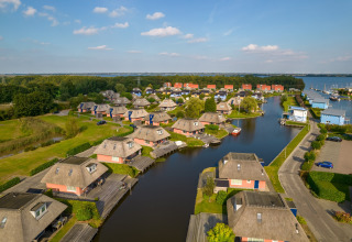 Vista aérea de cabañas vacacionales con techo de paja junto a un canal tranquilo y áreas verdes.