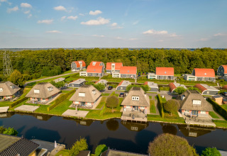 Luftaufnahme eines Ferienhausparks mit Strohdächern, Wasserläufen und viel Grün an einem Sonnentag.