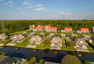 Luftaufnahme eines Ferienhausparks mit Strohdächern, Wasserläufen und viel Grün an einem Sonnentag.