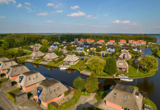 Luftaufnahme von malerischen Lodges mit Reetdächern an einem Kanal mit Booten und viel Grün.
