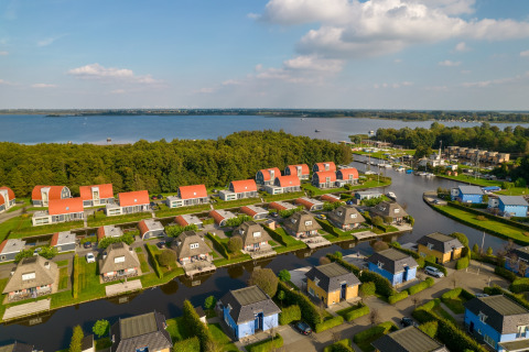Luftaufnahme von Lodges am See mit roten Dächern, viel Grün und angrenzendem Waldgebiet.
