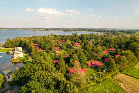 Aerial view of a scenic lakeside lodge, surrounded by trees and cabins with red roofs in green nature.