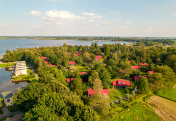 Aerial view of a scenic lakeside lodge, surrounded by trees and cabins with red roofs in green nature.