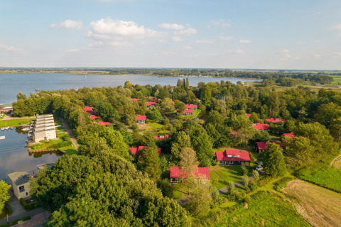 Luftaufnahme einer idyllischen Lodge am See, umgeben von vielen Bäumen und Häusern mit roten Dächern.