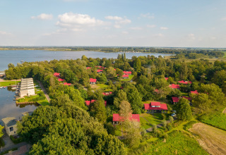 Aerial view of a scenic lakeside lodge, surrounded by trees and cabins with red roofs in green nature.