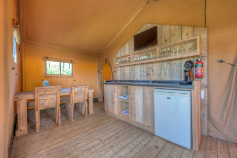 Interior of a safari tent with wooden furniture, kitchenette, and dining area at Holiday park Hunzedal 15, Netherlands.