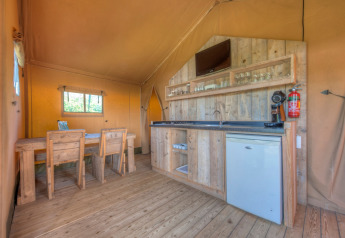 Interior de tienda safari con muebles de madera, cocina y zona comedor en Holiday park Hunzedal 15, Países Bajos.