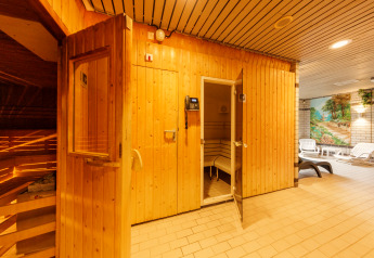 Entrada a una sauna de madera en una zona de relajación con tumbonas y mural pintado al fondo.