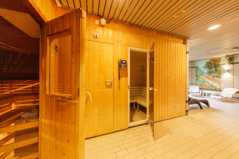 Ingresso a una sauna in legno in un'area relax con lettini e dipinto murale sullo sfondo.