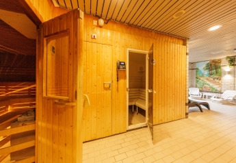 Entrada a una sauna de madera en una zona de relajación con tumbonas y mural pintado al fondo.
