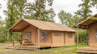 Safari tent with wooden terrace and picnic table at Holiday park Hunzedal, surrounded by greenery.