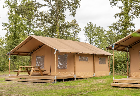 Safari tent with wooden terrace and picnic table at Holiday park Hunzedal, surrounded by greenery.