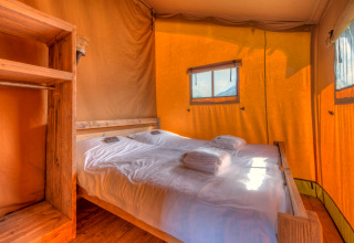 Interieur van een safaritent met dubbel bed en houten meubels in Holiday park Hunzedal 15.