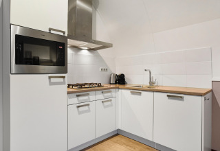 Moderne køkkenhjørne i Water park «De Bloemert 7» i Holland med hvide skabe og træbordplade.