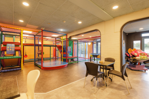 Zona de juegos interior con estructura para escalar, coche infantil y mesas en tienda safari familiar.