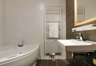 Bagno moderno con vasca ad angolo, lavandino a muro e scaldasalviette al Water park De Bloemert 7.