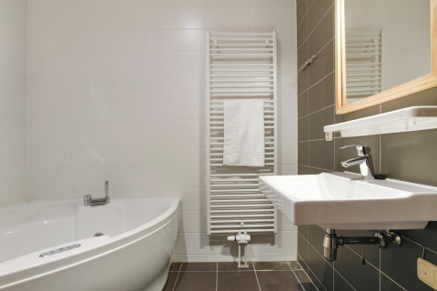 Bagno moderno con vasca ad angolo, lavandino a muro e scaldasalviette al Water park De Bloemert 7.