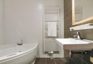 Modern bathroom with a corner bathtub, wall-mounted sink, and heated towel rack at Water park De Bloemert 7.