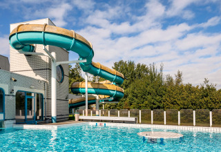 Buitenzwembad met grote kronkelende waterglijbaan aan een vrijetijdscentrum onder een bewolkte hemel.