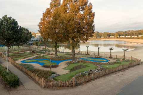 Foto van een minigolfbaan bij een meer, gezien vanaf een safaritent, omgeven door zand en bomen.