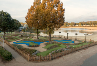 Foto van een minigolfbaan bij een meer, gezien vanaf een safaritent, omgeven door zand en bomen.