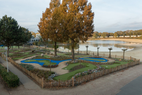 Photo of a mini-golf course by a lake, taken from a safari tent, with sand and trees surrounding it.