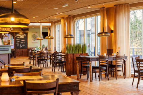 Gezellig en licht interieur van een safaritentrestaurant met houten meubels, planten en grote ramen.