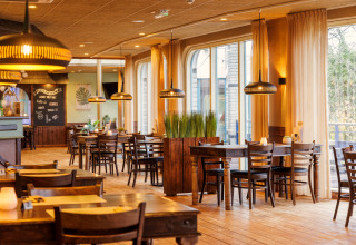 Licht, gezellig interieur van een safaritentrestaurant met houten tafels, stoelen en grote ramen met gordijnen.