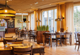 Intérieur lumineux de restaurant sous tente safari avec tables en bois, plantes vertes et grandes fenêtres.