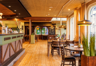 Binnenaanzicht van een gezellig restaurant met houten vloer, houten tafels en grote ramen met gordijnen.