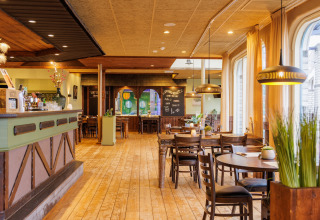 Innenaufnahme eines gemütlichen Restaurants mit Holzboden, Holzmöbeln und großen Fenstern mit Vorhängen.