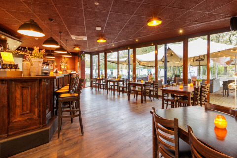 Indvendig udsigt til en hyggelig restaurant med træmøbler og bar, udsigt til telte udenfor.