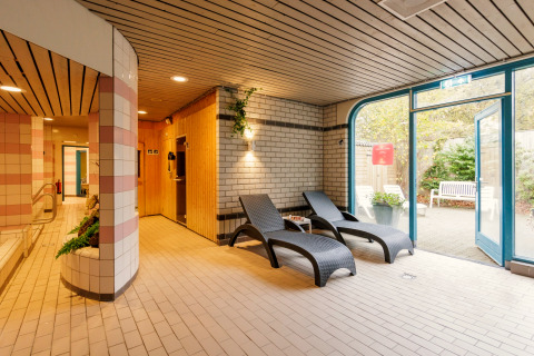 Binnenruimte van een safaritent met ligstoelen, sauna en toegang tot de tuin bij daglicht.