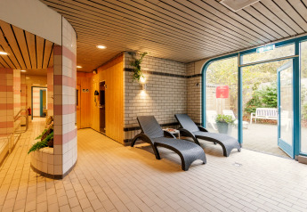 Binnenruimte van een safaritent met ligstoelen, sauna en toegang tot de tuin bij daglicht.