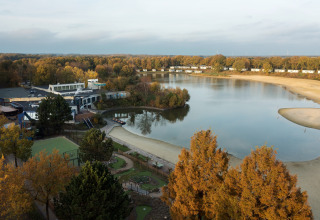 Vista di un lago con spiaggia sabbiosa, alberi autunnali e strutture vicino a una tenda safari.
