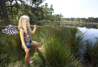 Mädchen mit Stock und Beutel erkundet am See das Gelände nahe eines Safarizeltes in der Natur.