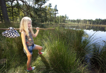 Niña con palo y fardo explora la orilla de un lago cerca de una tienda safari en plena naturaleza.
