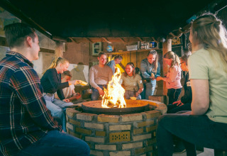 Een groep mensen rond een vuurkorf in een safaritent, samen genietend van een gezellige avond.