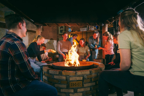 A group of people sitting around a firepit inside a safari tent, enjoying each other's company at night.