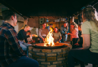 Eine Gruppe von Menschen sitzt gemütlich um ein Lagerfeuer in einem Safarizelt und lacht zusammen.