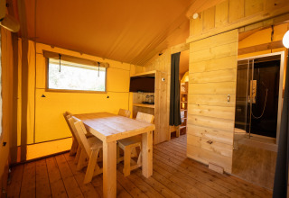 Vista interna della tenda safari al Holiday park «Hunzedal 16» con sala da pranzo, cucina e bagno.