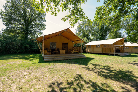 Safaritent op vakantiepark Hunzedal 16 in Nederland, omgeven door bomen en gras in het zonlicht.