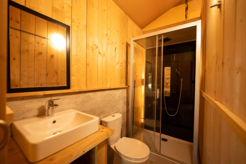 Baño en una tienda safari en Holiday park «Hunzedal 16» en los Países Bajos, con paredes de madera y ducha.