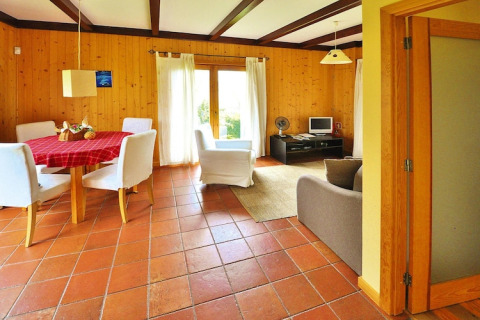 Lichte woonkamer van een bungalow in Portugal met houten wanden, eettafel, witte stoelen en grote ramen.