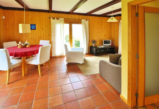 Lichte woonkamer van een bungalow in Portugal met houten wanden, eettafel, witte stoelen en grote ramen.