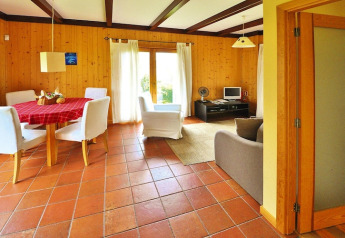Luminoso soggiorno in bungalow portoghese con pareti in legno, tavolo da pranzo, sedie bianche e ampie finestre.