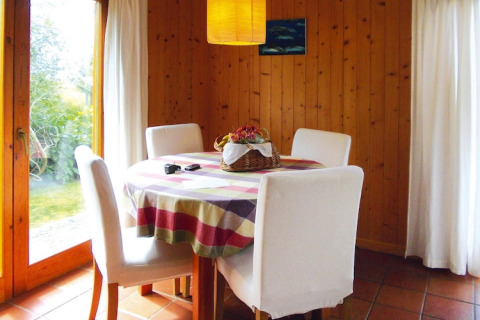 Eethoek in bungalow met ronde tafel, vier witte stoelen, kleurrijk tafelkleed en rieten mand als decoratie.