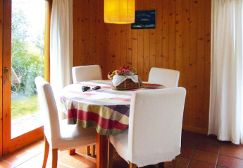 Zona pranzo in bungalow con tavolo rotondo, quattro sedie bianche, tovaglia colorata e centrotavola a cestino.