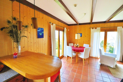 Lichte woonkamer in Portugees vakantiehuis met houten wanden, ronde eettafel en witte stoelen.