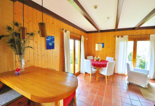 Lichte woonkamer in Portugees vakantiehuis met houten wanden, ronde eettafel en witte stoelen.
